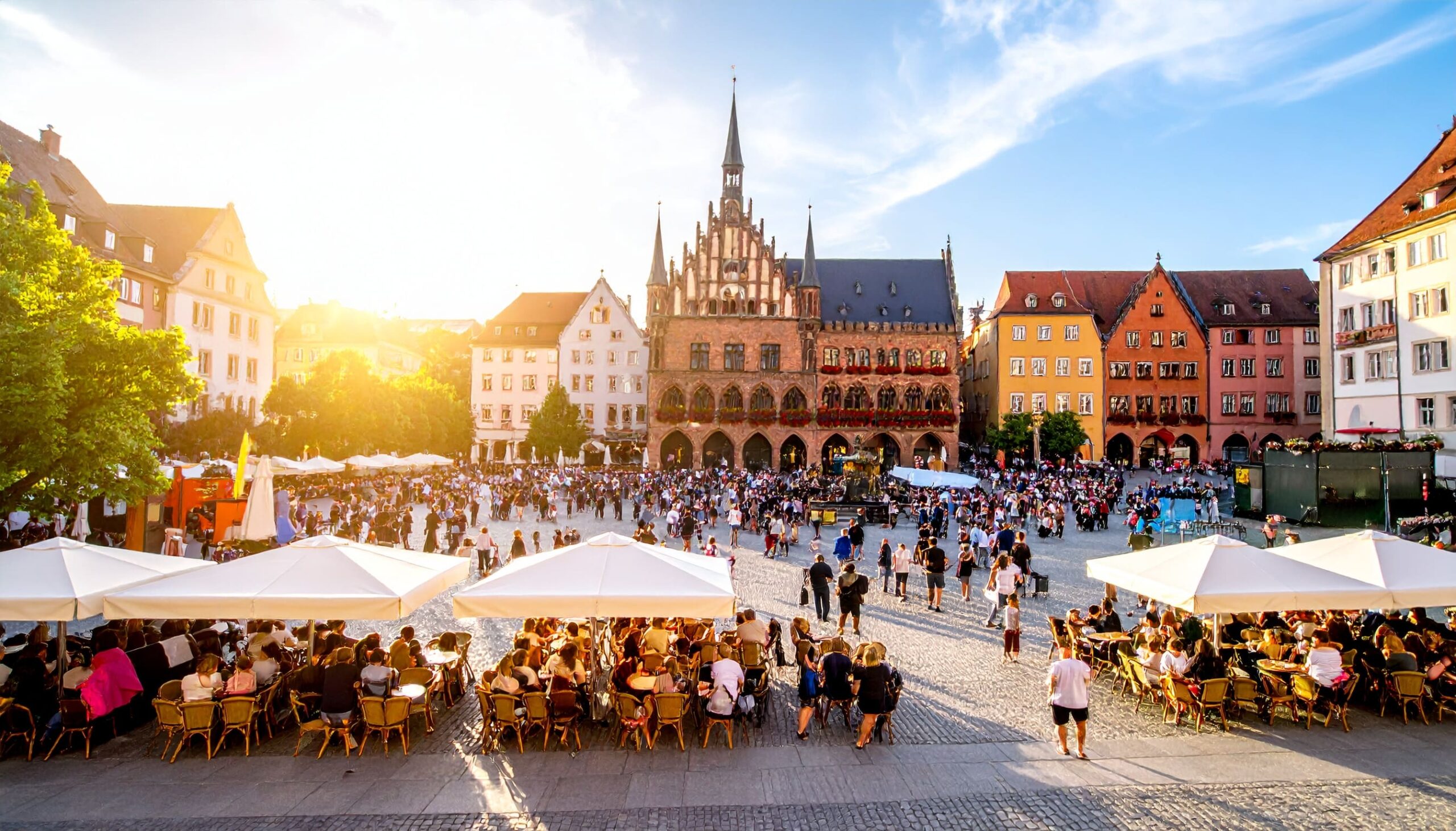 Lebhafter deutscher Stadtplatz bei Sonnenuntergang mit historischen Gebäuden, Straßencafés und kulturellen Darbietungen – die Vielfalt und Lebendigkeit der deutschen Kultur hautnah erleben.