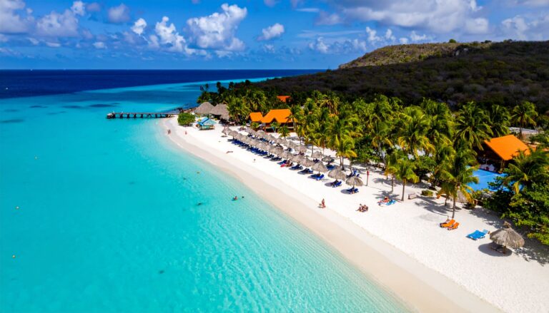 Atemberaubender Strand auf Curaçao mit türkisblauem Wasser, Palmen und bunten Strandhütten bei Sonnenschein