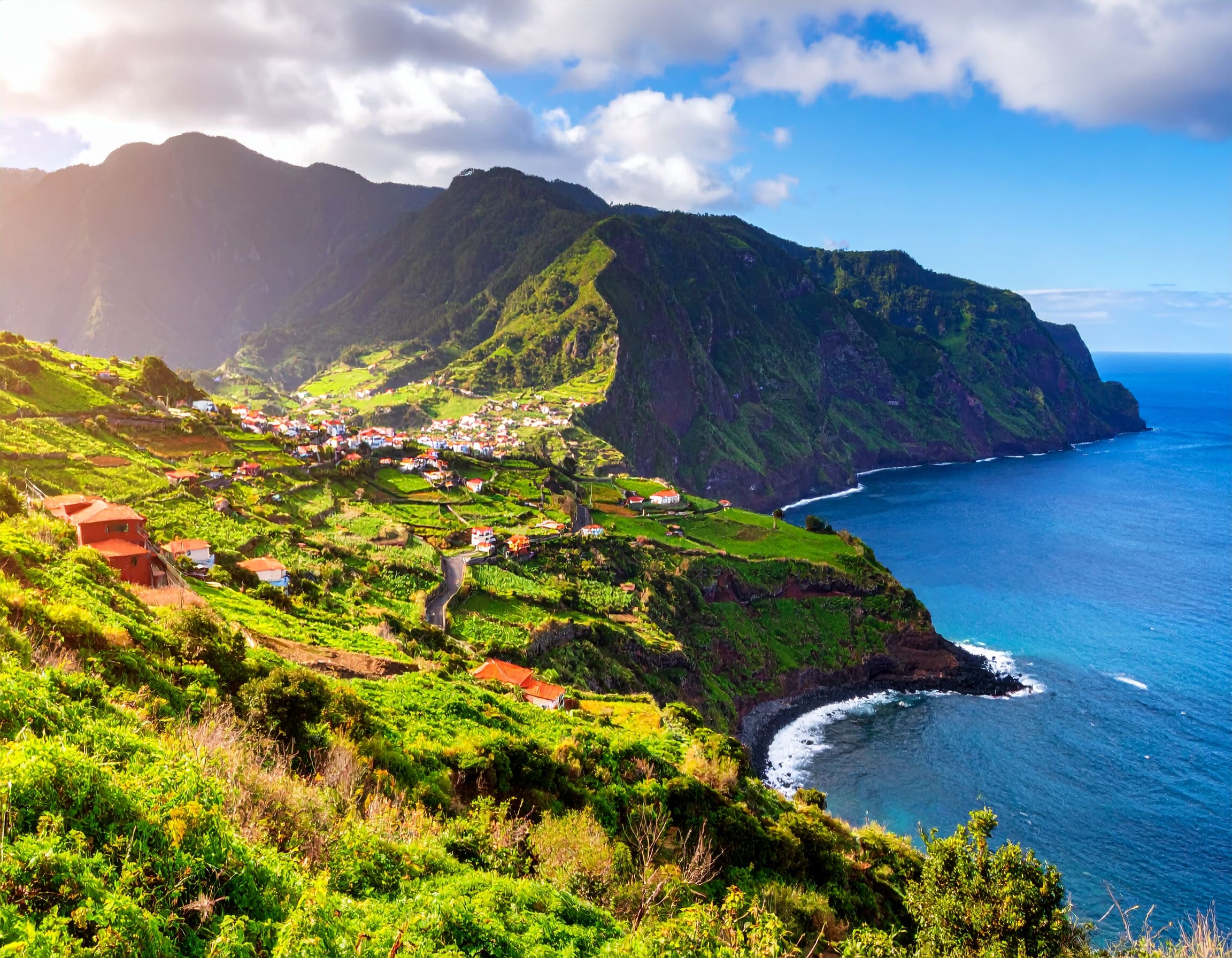Spektakuläre Vulkanlandschaft und Steilküste von Saba mit bunten Häusern und karibischem Meer im Hintergrund.