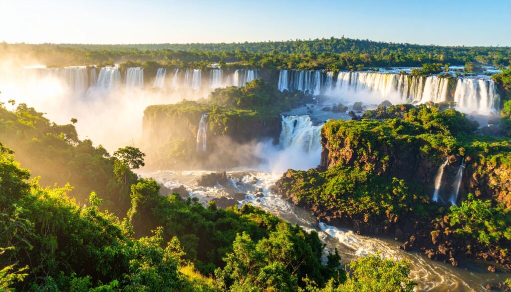 Eindrucksvolles Foto der Iguazú-Wasserfälle mit tropischem Regenwald und goldenem Morgenlicht.