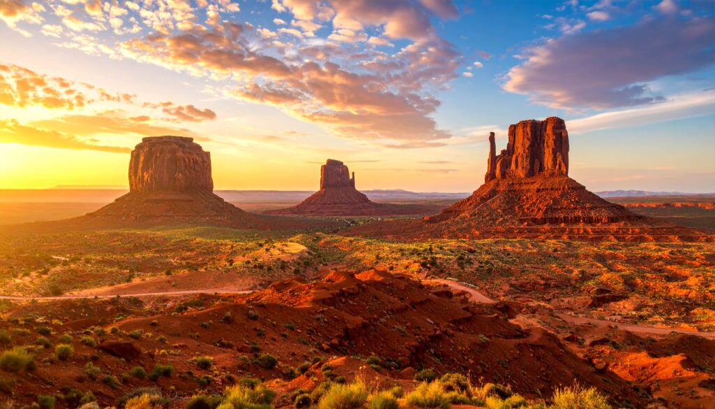 Sonnenaufgang über Monument Valley, rote Tafelberge leuchten im Morgenlicht.